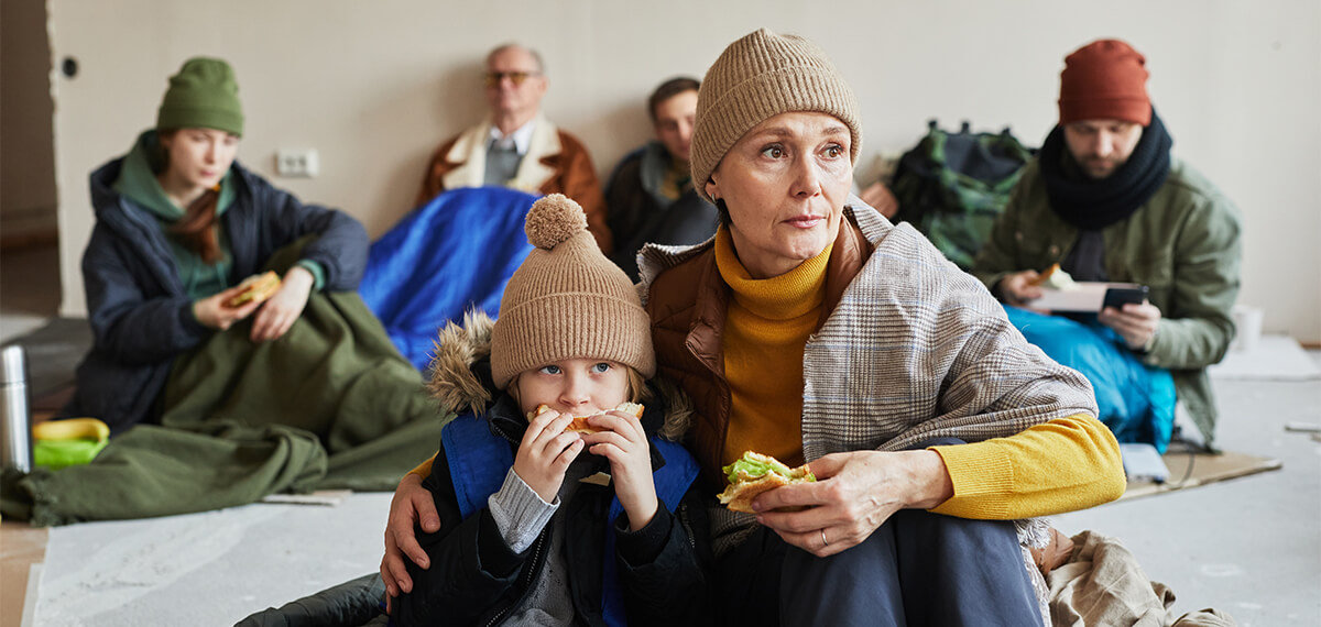 Woman sitting with her son in homeless shelter eating sandwiches.